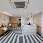 Reception area of a modern skin clinic with stylish black-and-white chevron flooring, peach walls, and a white tiled front desk, representing the Best Dermatologist in Financial District, Hyderabad